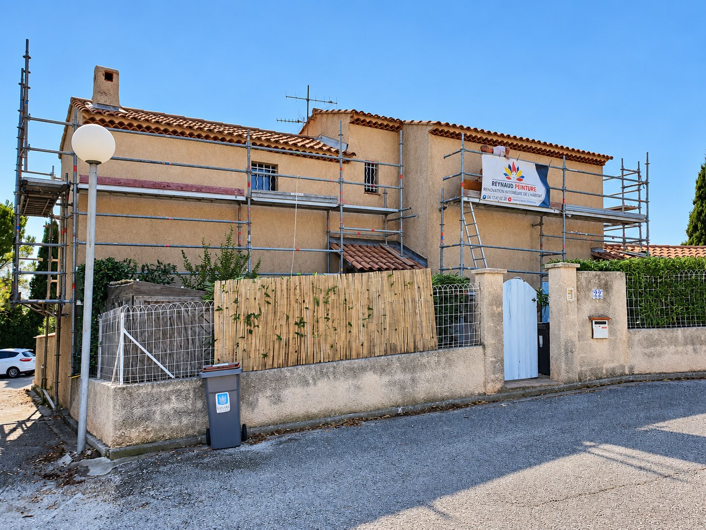 Façade d'une maison provençale entourée d'un échafaudage, avec une bâche publicitaire Reynaud Peinture accrochée sur le côté droit.